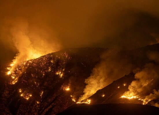 Intense wildfire blazing through mountains in California at night, creating a dramatic scene.
