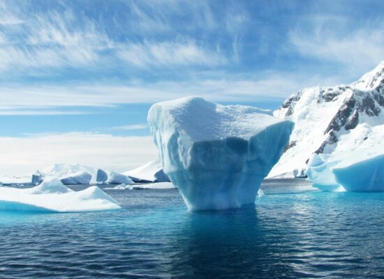 A stunning iceberg floating in the cold, pristine waters with a backdrop of snowy mountains.